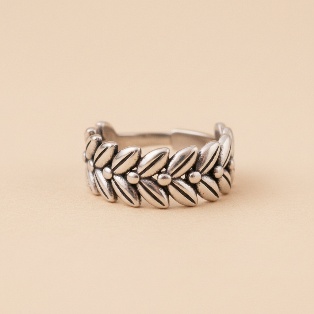 Anillo ajustable de acero con diseño de corona de laureles y espigas visto de frente sobre fondo beige
