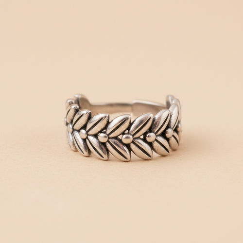 Anillo ajustable de acero con diseño de corona de laureles y espigas visto de frente sobre fondo beige